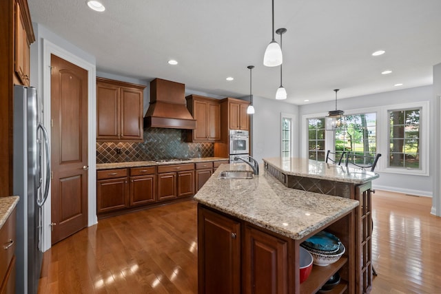 6820 Mahogany Dr, Galena, OH 43021 - kitchen featuring custom exhaust hood, appliances with stainless steel finishes, wood finished floors, a center island with sink, and backsplash