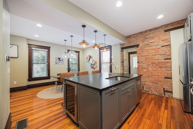 199 E Gates St, Columbus, OH 43206 - kitchen with brick wall, hardwood / wood-style flooring, wine cooler, appliances with stainless steel finishes, and an island with sink