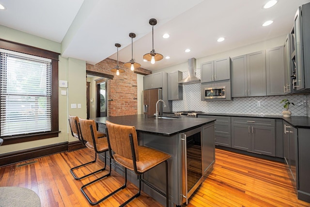 199 E Gates St, Columbus, OH 43206 - kitchen with wall chimney range hood, appliances with stainless steel finishes, wine cooler, dark countertops, and light wood-style flooring