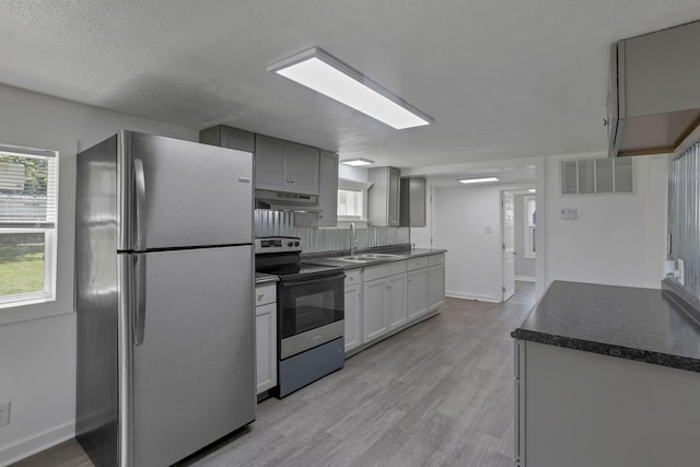8898 Baker Rd, Stoutsville, OH 43154 - kitchen with appliances with stainless steel finishes, under cabinet range hood, light wood-style floors, dark countertops, and a textured ceiling