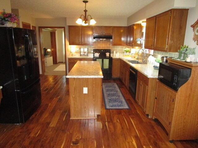 5669 Maplewood Ct, Lewis Center, OH 43035 - kitchen featuring black appliances, under cabinet range hood, a kitchen island, tasteful backsplash, and brown cabinets
