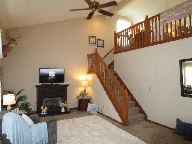 5669 Maplewood Ct, Lewis Center, OH 43035 - living room featuring high vaulted ceiling, carpet, a ceiling fan, stairs, and a glass covered fireplace