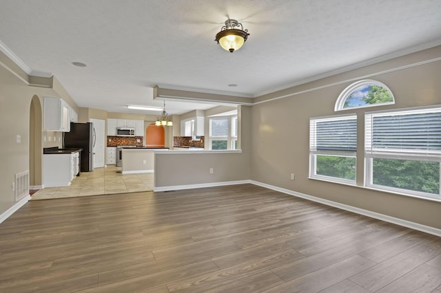 3902 Rivers Run Dr, Lewis Center, OH 43035 - unfurnished living room featuring crown molding, a chandelier, light wood-style floors, arched walkways, and a textured ceiling