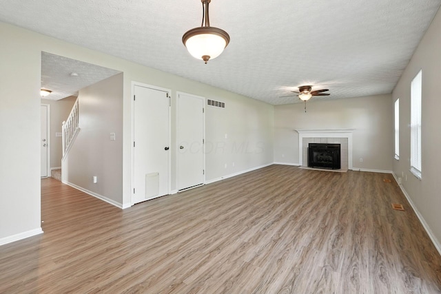 1771 Fern Trail Dr, Lancaster, OH 43130 - unfurnished living room featuring a textured ceiling, a ceiling fan, light wood finished floors, a fireplace, and stairs
