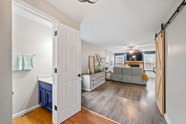 2387 Sutter Pkwy, Dublin, OH 43016 - bedroom featuring a barn door, light wood finished floors, a textured ceiling, a warm lit fireplace, and ceiling fan