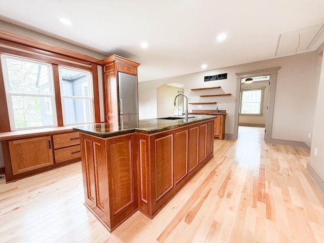 69 N Cherry St, Mount Gilead, OH 43338 - kitchen with arched walkways, brown cabinets, a center island with sink, light wood-style flooring, and stainless steel fridge