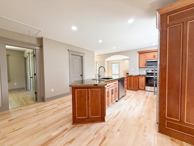 69 N Cherry St, Mount Gilead, OH 43338 - kitchen featuring appliances with stainless steel finishes, brown cabinetry, a center island with sink, light wood-style flooring, and arched walkways