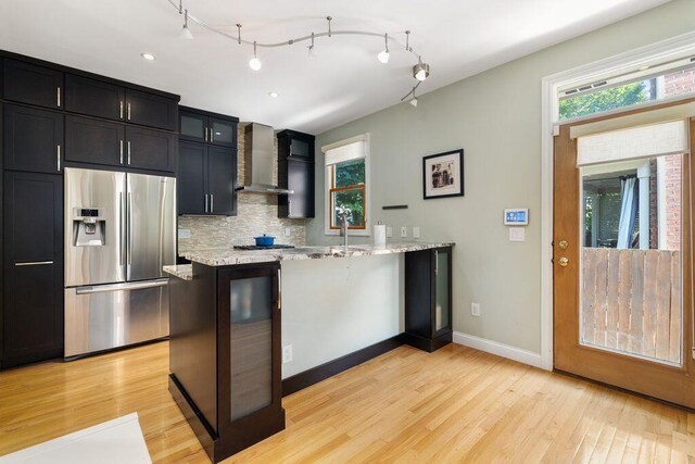 979 Delaware Ave, Columbus, OH 43201 - kitchen featuring stainless steel fridge with ice dispenser, wall chimney range hood, dark cabinets, and light wood finished floors