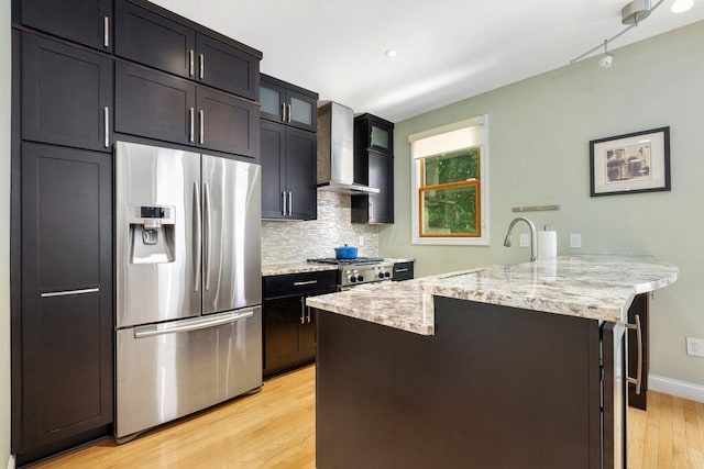 979 Delaware Ave, Columbus, OH 43201 - kitchen featuring stainless steel refrigerator with ice dispenser, a peninsula, wall chimney range hood, light wood finished floors, and light stone counters