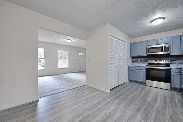 1142 Rozelle Creek Rd, Chillicothe, OH 45601 - kitchen featuring appliances with stainless steel finishes, a textured ceiling, light wood-type flooring, open floor plan, and backsplash