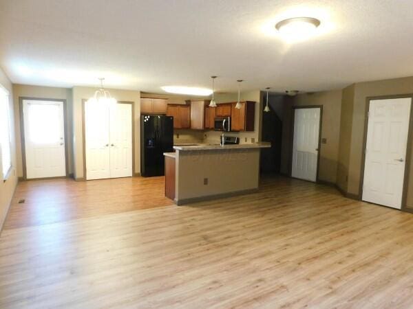 32340 Lilac Ln, Logan, OH 43138 - kitchen with black refrigerator with ice dispenser, stainless steel microwave, open floor plan, light wood-style flooring, and decorative light fixtures