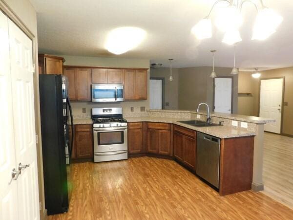 32340 Lilac Ln, Logan, OH 43138 - kitchen featuring appliances with stainless steel finishes, a peninsula, light wood-style flooring, brown cabinets, and light stone countertops