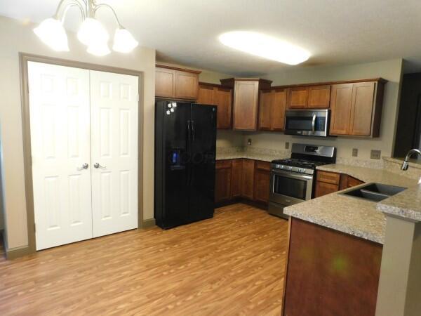 32340 Lilac Ln, Logan, OH 43138 - kitchen with appliances with stainless steel finishes, light wood finished floors, a peninsula, a chandelier, and brown cabinetry