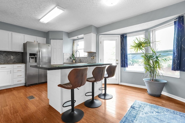 5683 Levi Kramer Blvd, Canal Winchester, OH 43110 - kitchen featuring stainless steel fridge, a breakfast bar, dark countertops, white cabinetry, and a textured ceiling