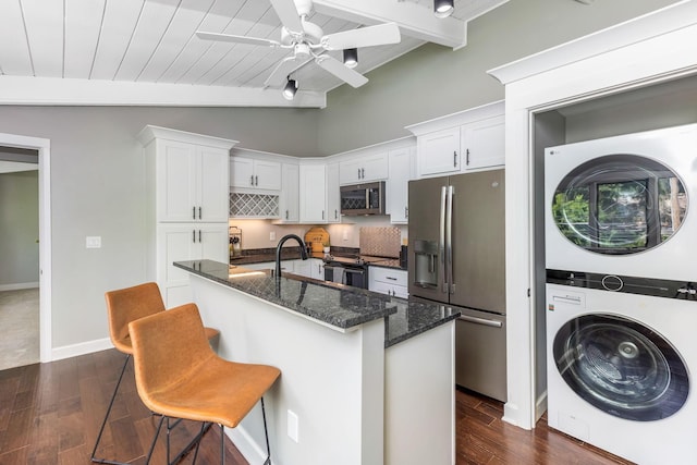 2109 W 5th Ave Unit C, Grandview Heights, OH 43212 - kitchen featuring appliances with stainless steel finishes, estacked washer and dryer, dark wood-style flooring, white cabinetry, and dark stone countertops