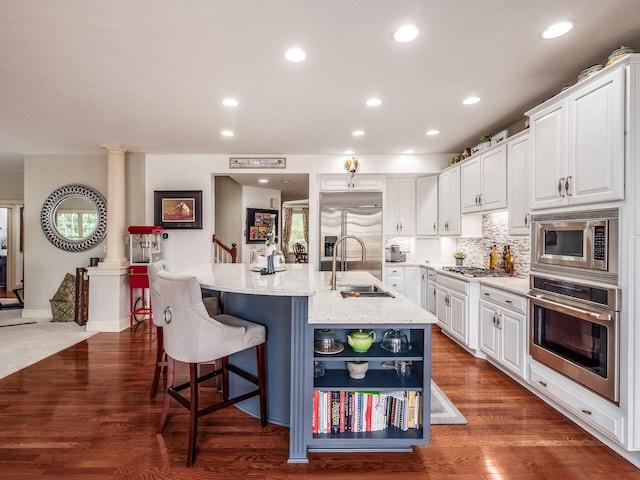 6676 Ballantrae Pl, Dublin, OH 43016 - kitchen featuring built in appliances, white cabinetry, a kitchen island with sink, a kitchen bar, and light stone countertops