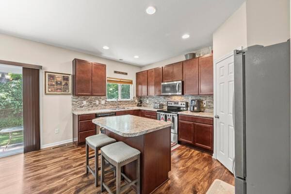 3810 Winding Path Dr, Canal Winchester, OH 43110 - kitchen featuring appliances with stainless steel finishes, decorative backsplash, dark wood-style floors, light countertops, and a breakfast bar area