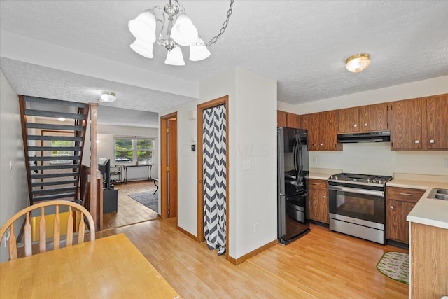 907 Soramill Ln Unit 8E, Columbus, OH 43085 - kitchen featuring stainless steel gas range, under cabinet range hood, freestanding refrigerator, a chandelier, and light wood finished floors