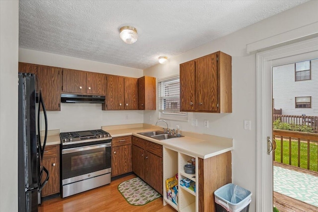 907 Soramill Ln Unit 8E, Columbus, OH 43085 - kitchen featuring stainless steel gas stove, freestanding refrigerator, under cabinet range hood, brown cabinetry, and a textured ceiling