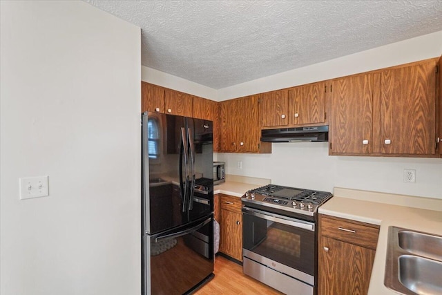 907 Soramill Ln Unit 8E, Columbus, OH 43085 - kitchen featuring freestanding refrigerator, stainless steel range with gas cooktop, under cabinet range hood, light countertops, and brown cabinetry