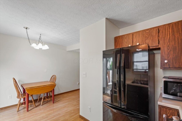 907 Soramill Ln Unit 8E, Columbus, OH 43085 - kitchen featuring freestanding refrigerator, stainless steel microwave, a textured ceiling, light wood-type flooring, and a chandelier