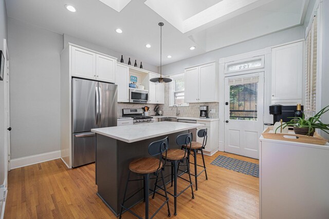 133 E Sycamore St, Columbus, OH 43206 - kitchen featuring stainless steel appliances, a skylight, light wood-type flooring, white cabinets, and a kitchen bar
