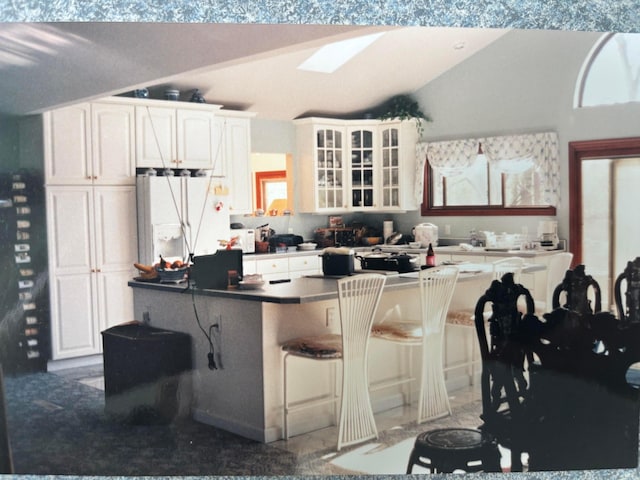 3535 Polley Rd, Columbus, OH 43221 - kitchen featuring freestanding refrigerator, lofted ceiling, glass insert cabinets, white cabinets, and a kitchen bar