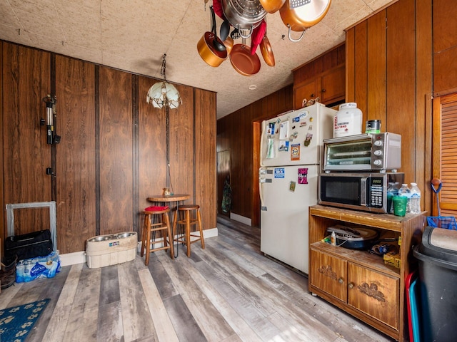 775 Koebel Ave, Columbus, OH 43207 - kitchen featuring freestanding refrigerator, stainless steel microwave, light wood finished floors, wood walls, and brown cabinetry