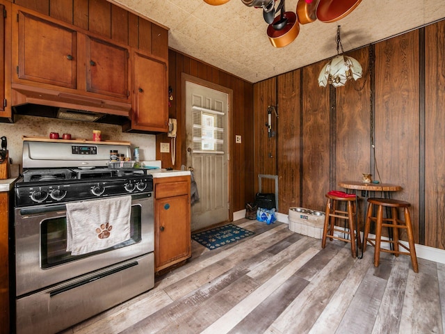 775 Koebel Ave, Columbus, OH 43207 - kitchen featuring gas range, under cabinet range hood, light countertops, light wood-style floors, and wood walls