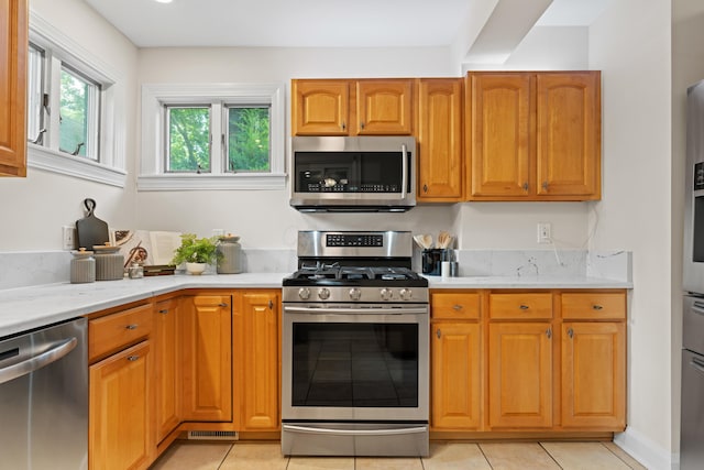 99 E N Broadway St, Columbus, OH 43214 - kitchen with stainless steel appliances, brown cabinetry, light stone counters, and light tile patterned floors