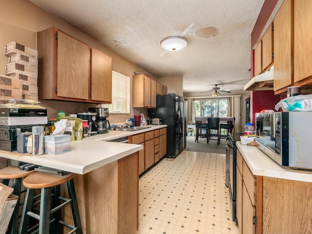 2883 Castlebrook Ave, Hilliard, OH 43026 - kitchen featuring black appliances, under cabinet range hood, a peninsula, a textured ceiling, and ceiling fan