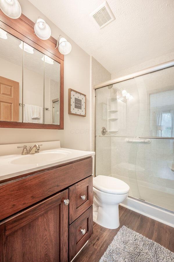 2621 Edencreek Ln, Columbus, OH 43207 - full bath featuring wood finished floors, vanity, a stall shower, and a textured ceiling