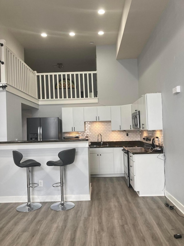 1276 N High St Unit 206, Columbus, OH 43201 - kitchen with stainless steel appliances, dark countertops, dark wood-type flooring, white cabinetry, and a high ceiling