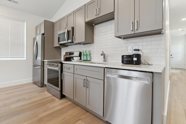 875 Bellows Ave, Columbus, OH 43223 - kitchen featuring stainless steel appliances, gray cabinets, light wood finished floors, backsplash, and vaulted ceiling
