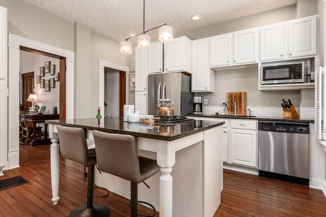 482 E Whittier St, Columbus, OH 43206 - kitchen featuring stainless steel appliances, a kitchen island, a breakfast bar, white cabinetry, and dark wood-style flooring