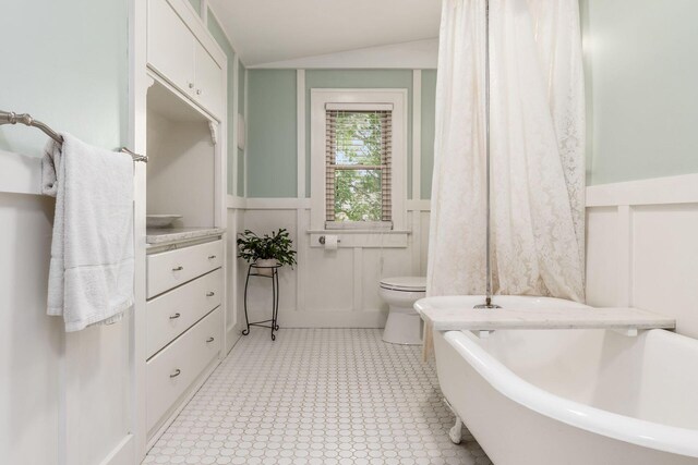 482 E Whittier St, Columbus, OH 43206 - bathroom with a bathtub, a wainscoted wall, vaulted ceiling, a decorative wall, and tile patterned floors