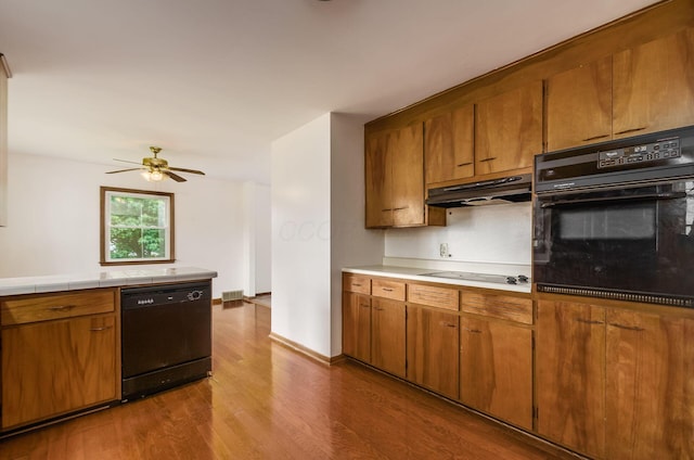 5930 Coonpath Rd NW, Carroll, OH 43112 - kitchen featuring black appliances, under cabinet range hood, dark wood-style flooring, brown cabinets, and a ceiling fan