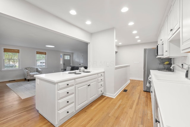 2560 Zollinger Rd, Columbus, OH 43221 - kitchen featuring white cabinetry, light countertops, a peninsula, light wood-style flooring, and decorative backsplash