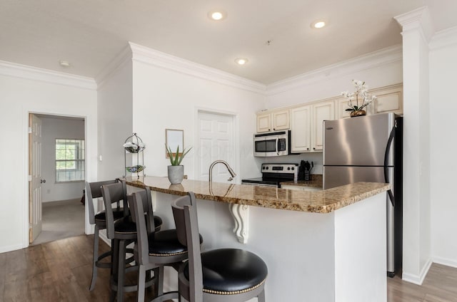6065 Craughwell Ln, Dublin, OH 43017 - kitchen featuring appliances with stainless steel finishes, cream cabinetry, wood finished floors, a kitchen breakfast bar, and ornamental molding