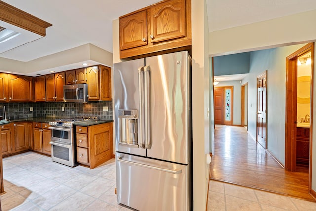 175 Academy Woods Dr, Columbus, OH 43230 - kitchen featuring appliances with stainless steel finishes, brown cabinetry, light tile patterned floors, dark countertops, and tasteful backsplash