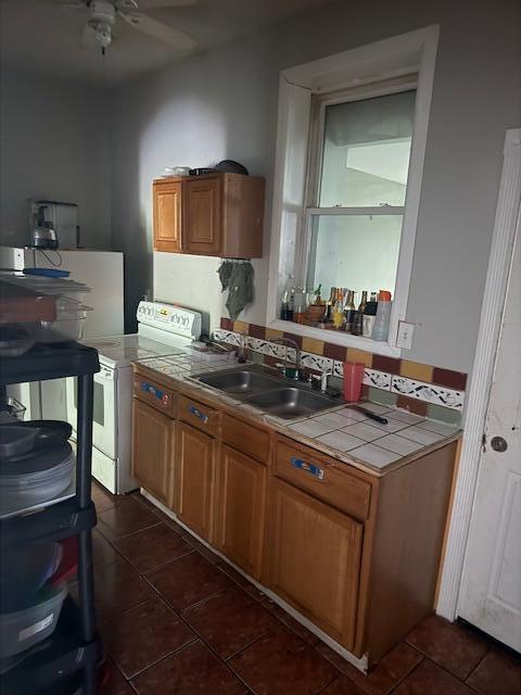 1364 E Fulton St, Columbus, OH 43205 - kitchen featuring tile counters, white range with electric cooktop, dark tile patterned floors, a ceiling fan, and brown cabinetry