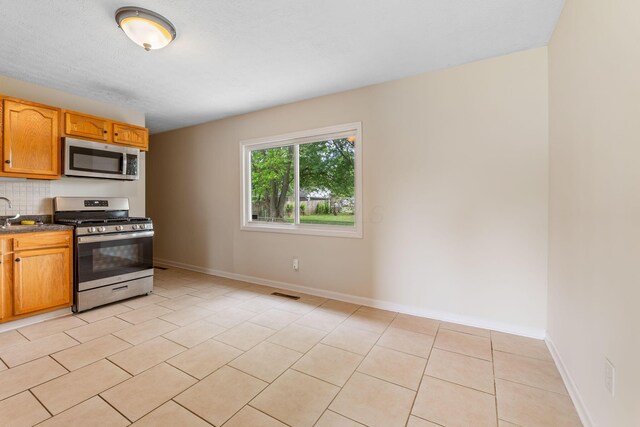 893 Aladdin Ct, Columbus, OH 43207 - kitchen with appliances with stainless steel finishes, decorative backsplash, light tile patterned flooring, and brown cabinetry