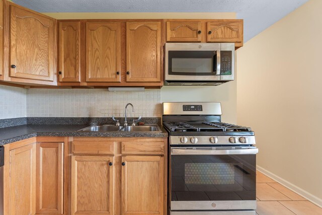 893 Aladdin Ct, Columbus, OH 43207 - kitchen featuring appliances with stainless steel finishes, light tile patterned floors, dark countertops, backsplash, and brown cabinets