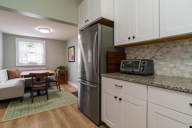 2686 Wicklow Rd, Columbus, OH 43204 - kitchen with light wood-type flooring, decorative backsplash, freestanding refrigerator, dark stone counters, and white cabinetry