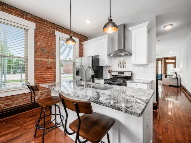119 Miami Ave Unit 119, Columbus, OH 43203 - kitchen with wall chimney range hood, stainless steel appliances, dark wood-style flooring, brick wall, and white cabinets