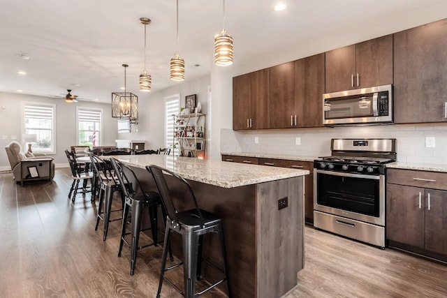 1232 N Grant Ave, Columbus, OH 43201 - kitchen featuring appliances with stainless steel finishes, a kitchen bar, light wood-style flooring, backsplash, and recessed lighting