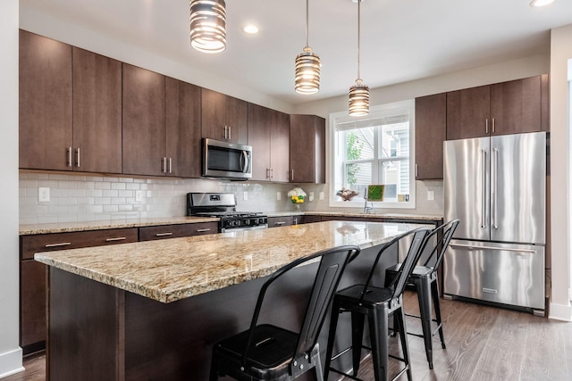 1232 N Grant Ave, Columbus, OH 43201 - kitchen featuring appliances with stainless steel finishes, wood finished floors, a breakfast bar, dark brown cabinetry, and recessed lighting