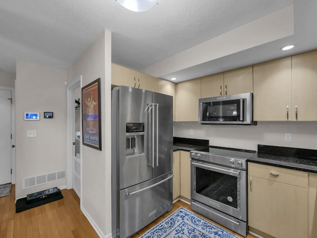 1235 Shagbark Rd, Columbus, OH 43230 - kitchen featuring appliances with stainless steel finishes, cream cabinetry, light wood-type flooring, light brown cabinetry, and a textured ceiling