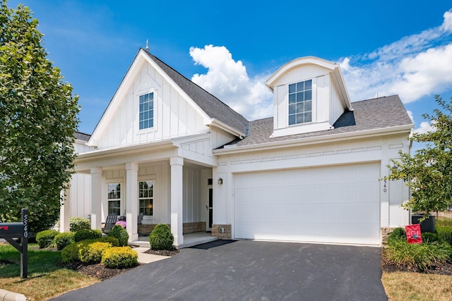 5540 Eva Loop S, Dublin, OH 43016 - view of front facade with board and batten siding, covered porch, asphalt driveway, a shingled roof, and stone siding