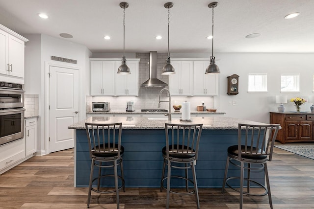 5540 Eva Loop S, Dublin, OH 43016 - kitchen featuring wall chimney range hood, appliances with stainless steel finishes, decorative backsplash, an island with sink, and recessed lighting